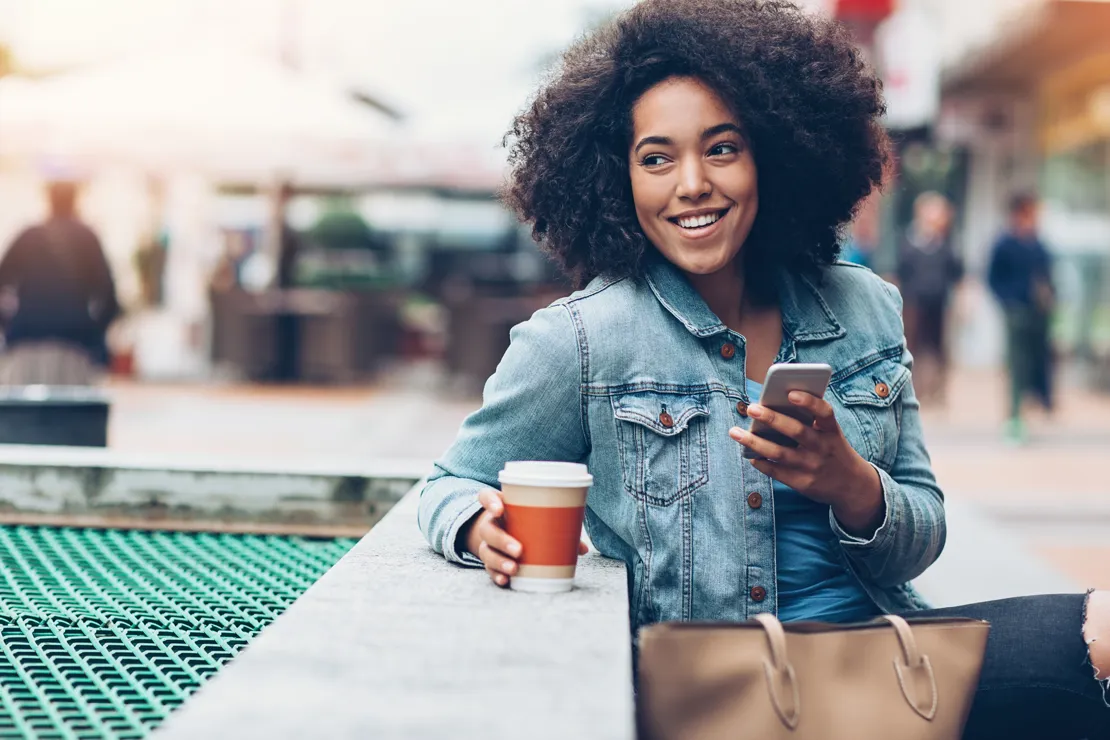 Woman Smiling On A Bench As She Looks At Her Phone
