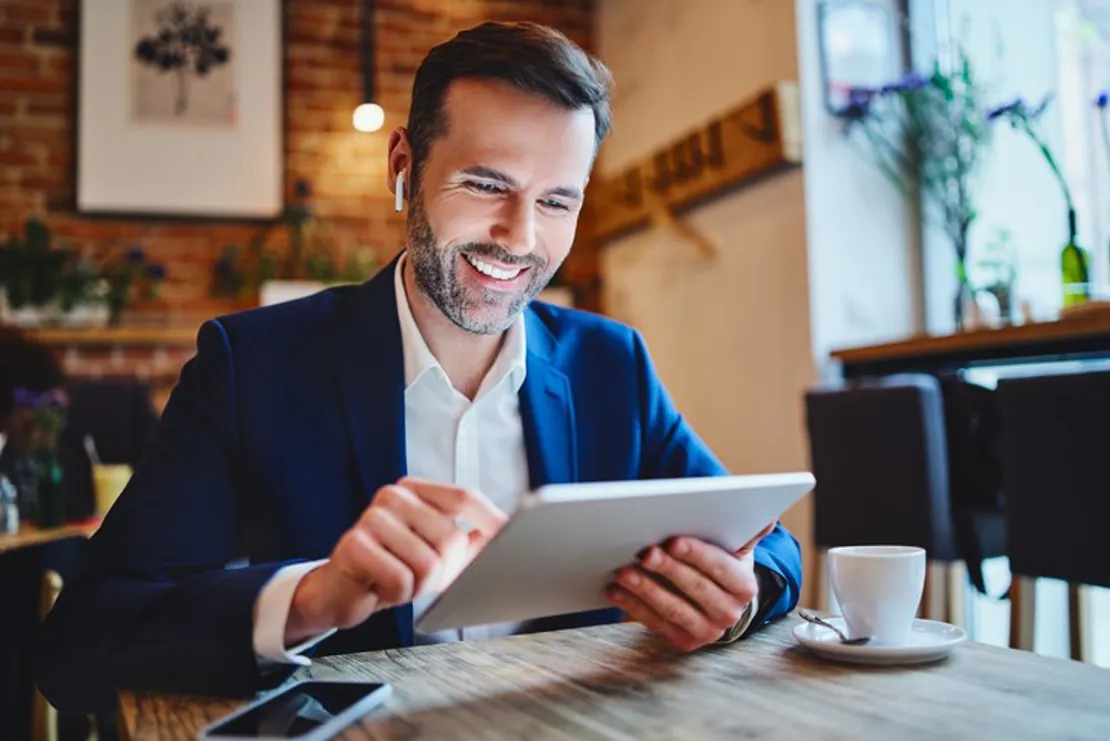 Businessman Sitting In Cafe Looking At Tablet During Phone Call